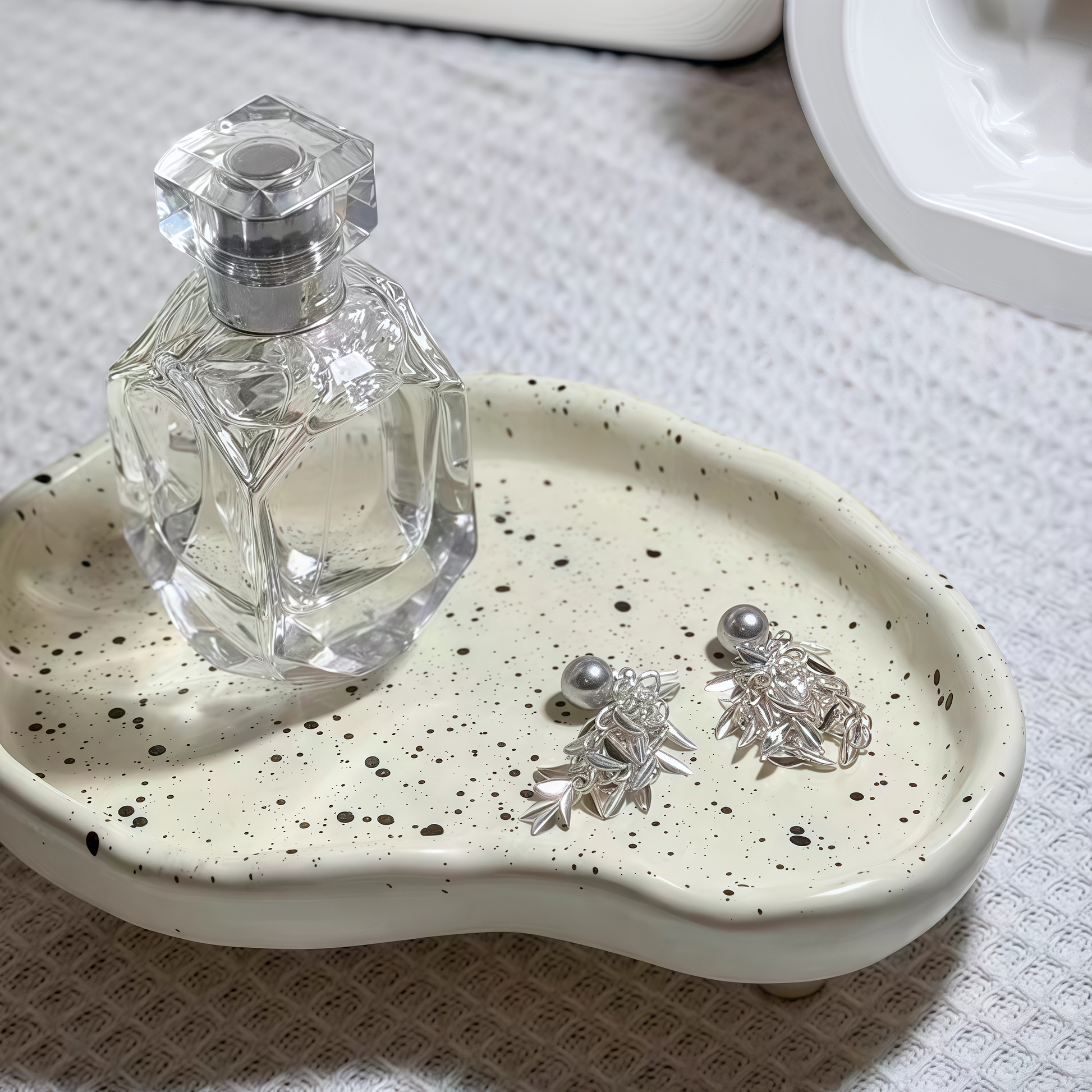 Ceramic splatter tray organizing perfumes, cosmetics, and jewelry on a vanity table."