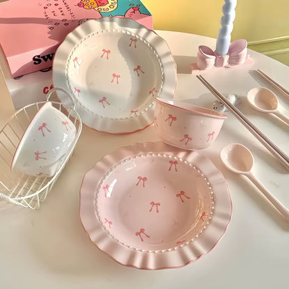 pink and white ceramic tableware set with bow patterns on a light surface.