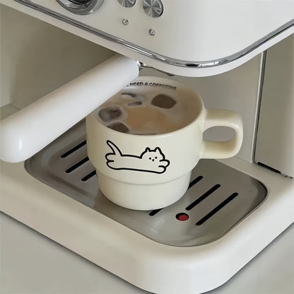 White coffee cup with a cat design on an espresso machine.