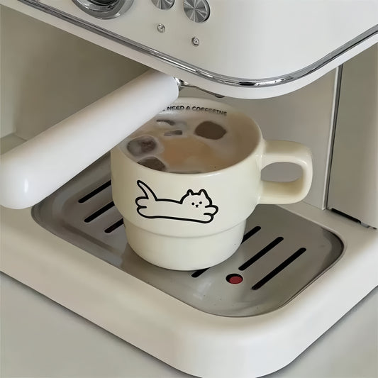 White coffee cup with a cat design on an espresso machine.