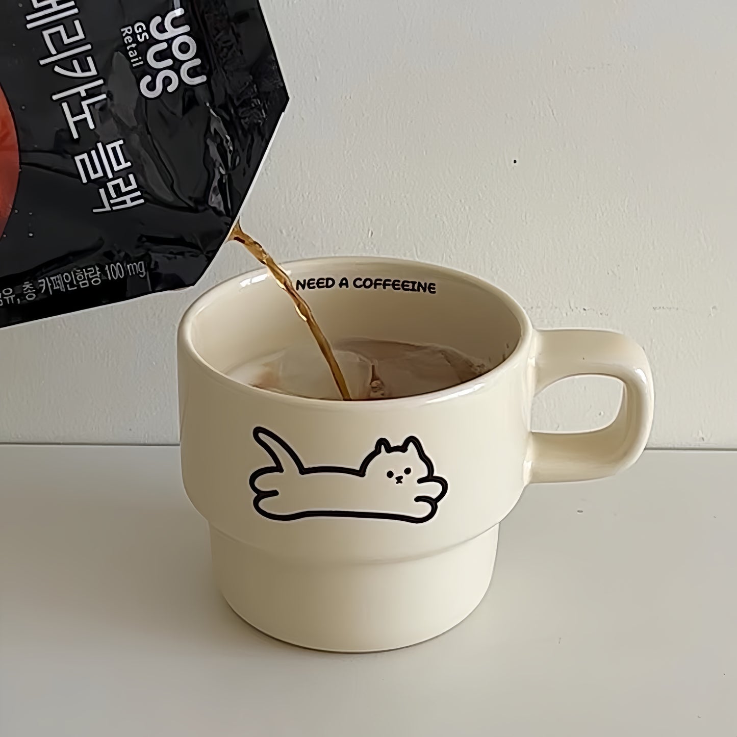White mug with a cat illustration being filled with coffee, next to a coffee bag.