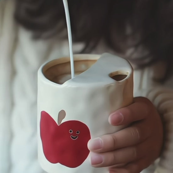 A set of handmade ceramic travel mugs shown from different angles, highlighting the unique apple artwork.