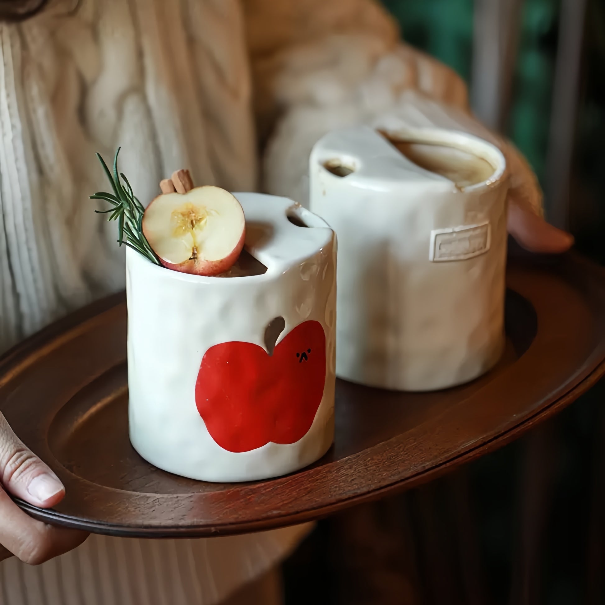 An artist's hand meticulously hand-painting the apple design on the ceramic travel mug.