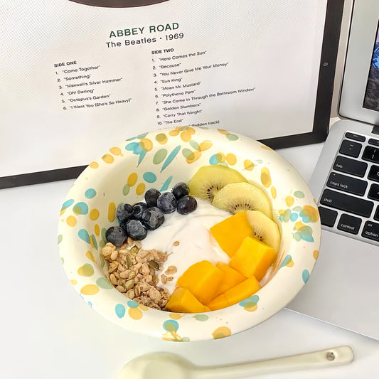 Splatter-glazed ceramic bowl filled with colorful cereal and milk on a wooden table.