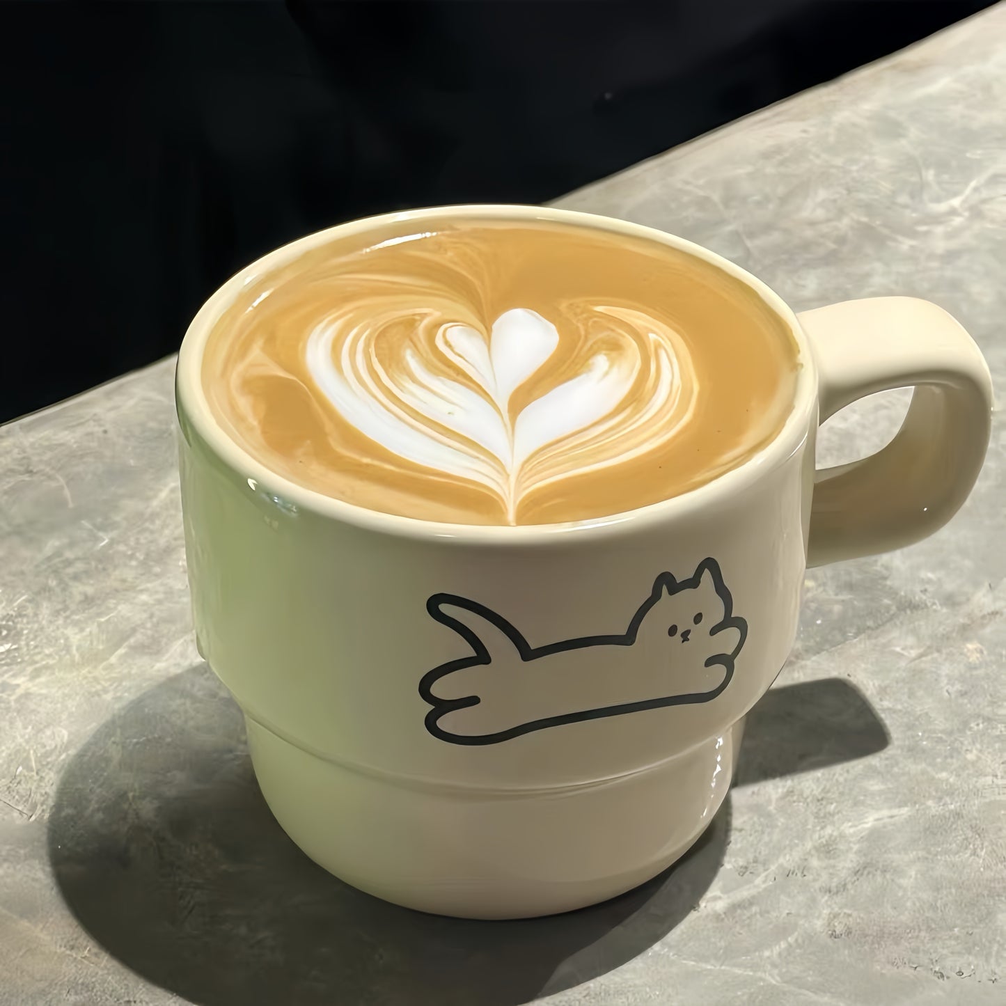 Ceramic mug with a cat illustration on a surface with a latte art design.